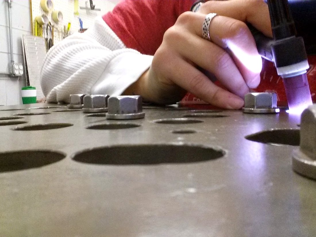 Hands steadying a small part under a torch on a fixture at a shop bench