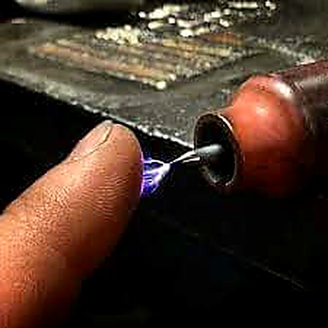 A hand steadying a small part under a torch arc on a shop bench
