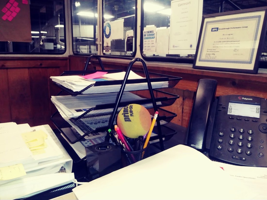 A shop office desk stacked with paper trays, forms, sticky notes and a phone